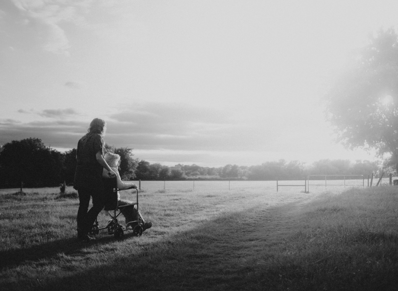 person pushing another in a wheelchair down a beautiful outdoor path.